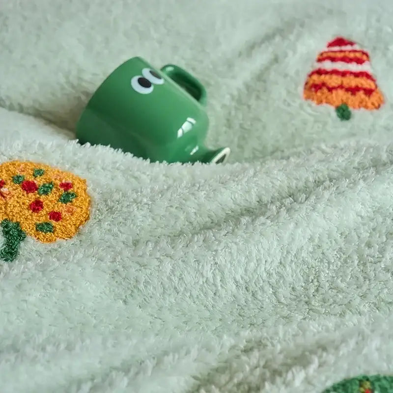 A green ceramic mug with googly eyes peeks from under a white towel on a mint green matte ant velvet duvet set