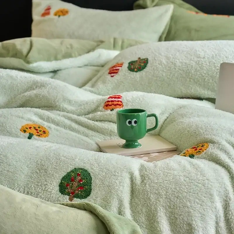 A green ceramic mug with googly eyes on a wooden coaster on a mint green embroidered matte ant velvet duvet set blanket