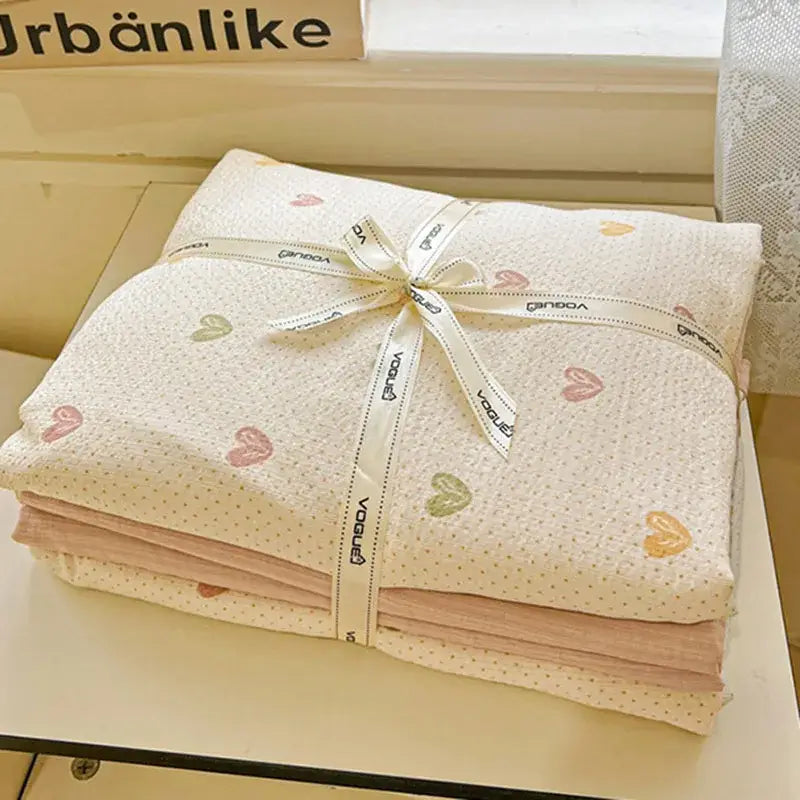A neatly folded stack of cream cotton muslin blankets with pastel hearts in a mint green floral double layer duvet cover set