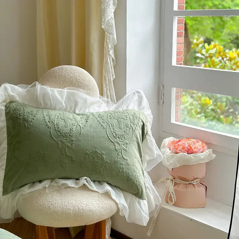 A soft sage green rectangular pillow with embroidered floral patterns and ruffled trim in a french carved velvet bedding set