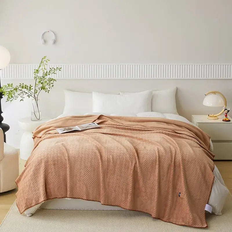 A rust-colored soft throw blanket with woven pattern and pom-pom trim made of jacquard milk velvet decorbites