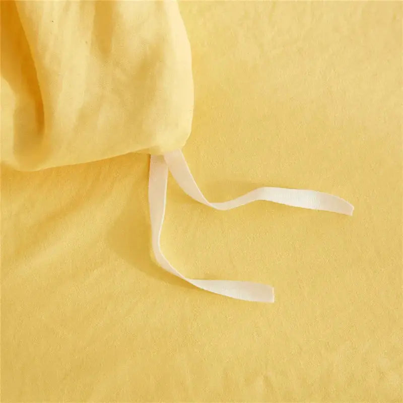 Soft yellow linen fabric with white drawstrings as part of a mint green quilted duvet cover set with pom pom trim