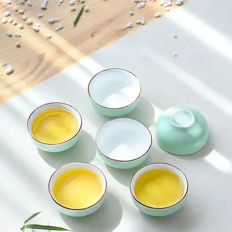 Set of five mint green and white celadon tea cups with gold rims holding golden-yellow liquid decorbites celadon tea cup set