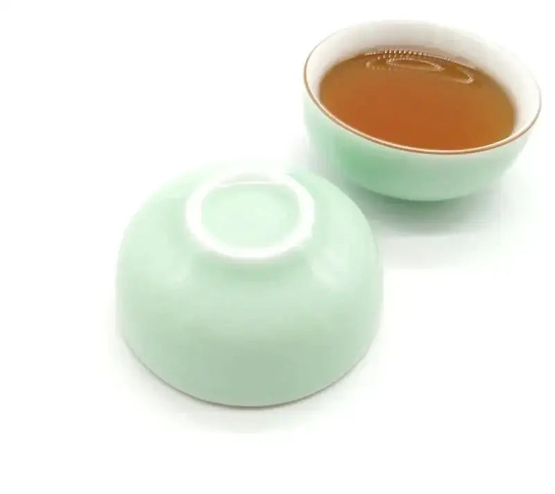 A mint green and white celadon tea cup set with gold rim porcelain filled with amber brewed tea by decorbites celadon tea