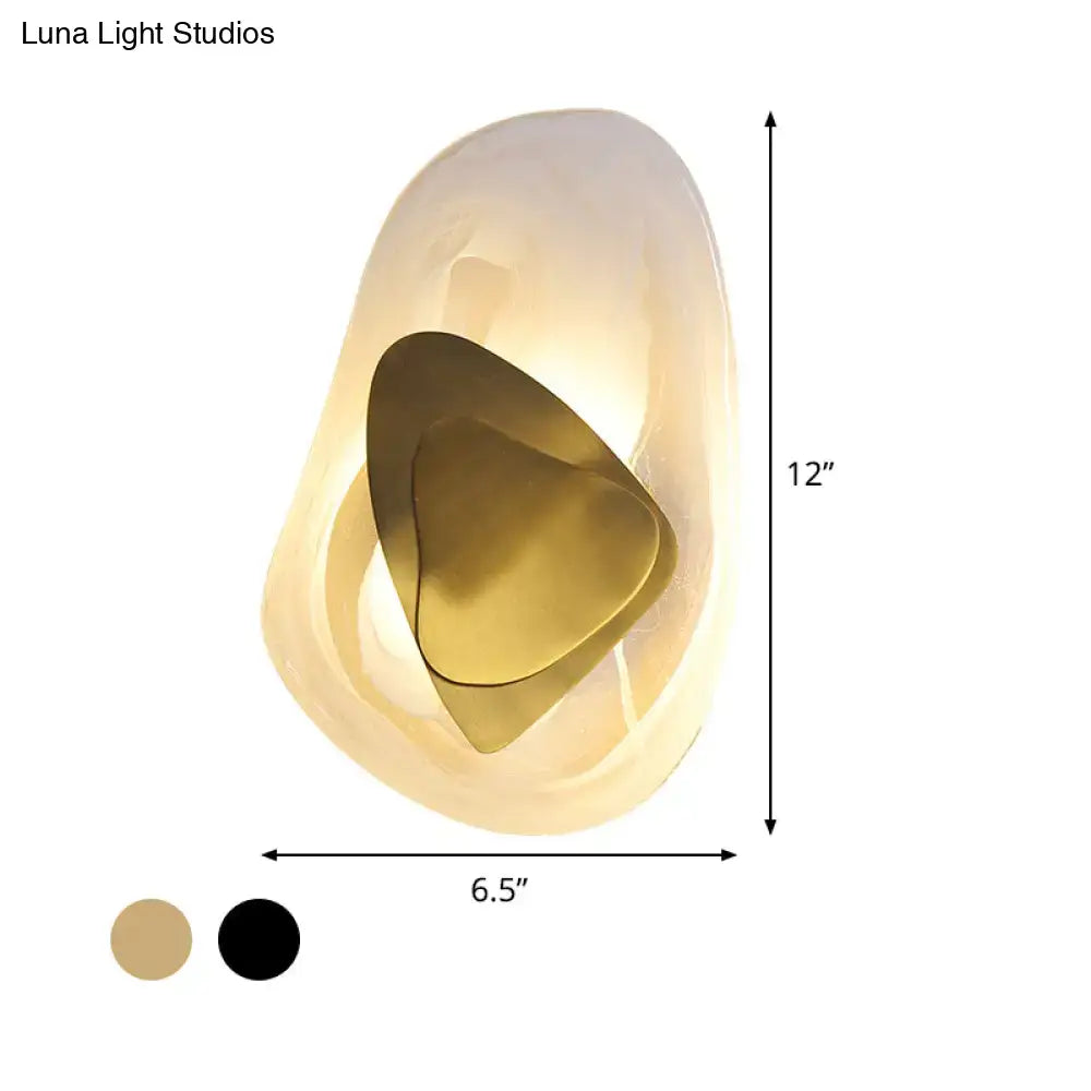A modern abstract clear glass rock wall sconce with translucent off-white shell and gold inner layer for dining room lighting