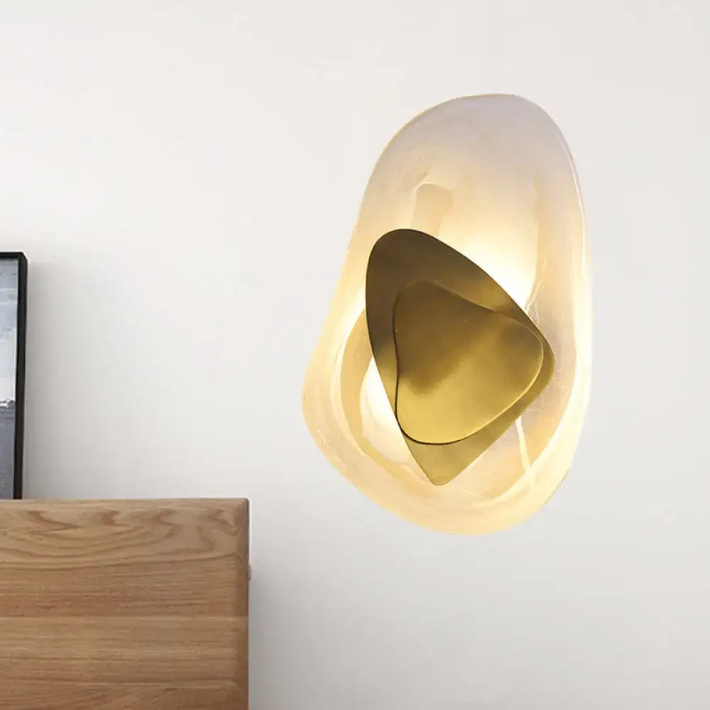 Modern abstract clear glass rock wall sconce with a warm-glowing translucent shell and polished brass for dining room use