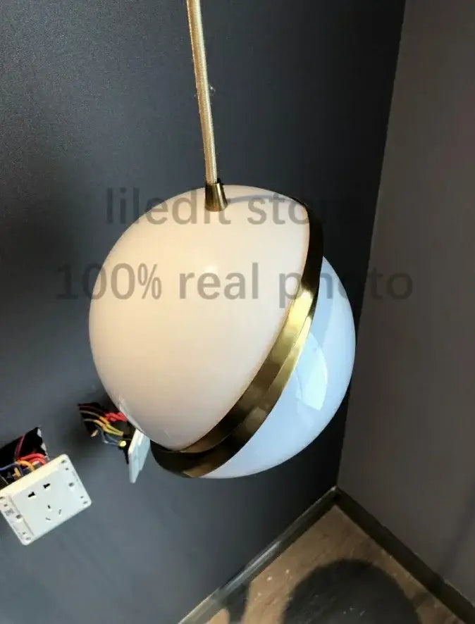 A modern acrylic ball pendant lamp with frosted white glass globe and polished brass accent for living room lighting