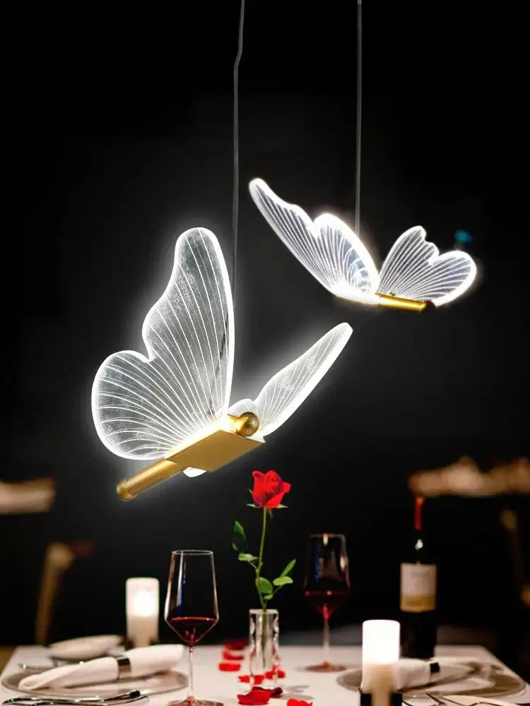 Two modern acrylic butterfly led chandelier pendant lights with translucent wings and gold bodies above dining table