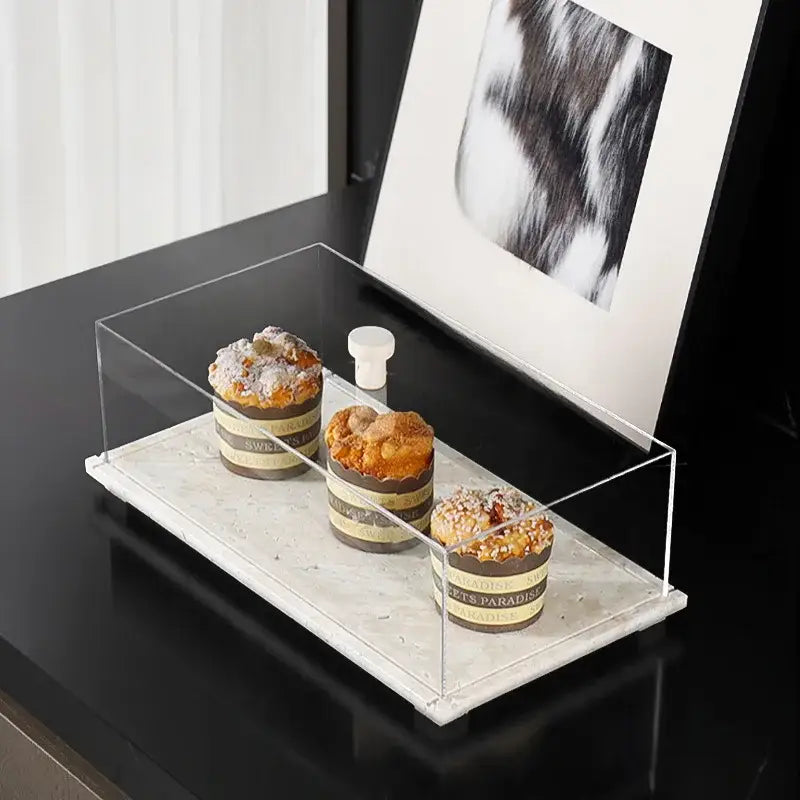 Modern acrylic display case with a clear acrylic display case and white travertine base holding chocolate pastries