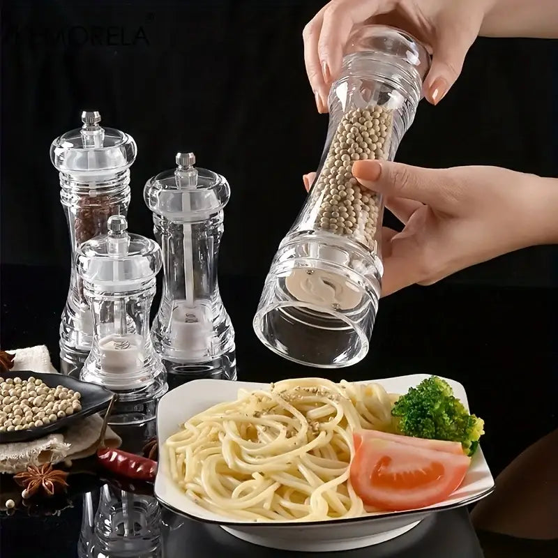 Clear glass decorbites acrylic manual pepper grinder filled with white peppercorns held above pasta plate for seasoning