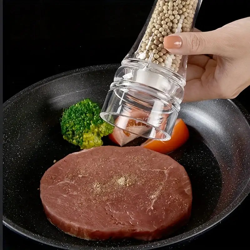 Modern decorbites acrylic manual pepper grinder filled with white peppercorns over sizzling steak in black pan
