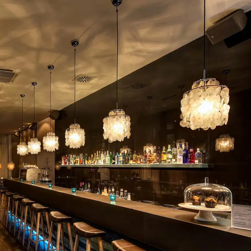 Delicate warm glowing decorbites aeolian bells shell chandelier pendant lights hang in elegant bar setting