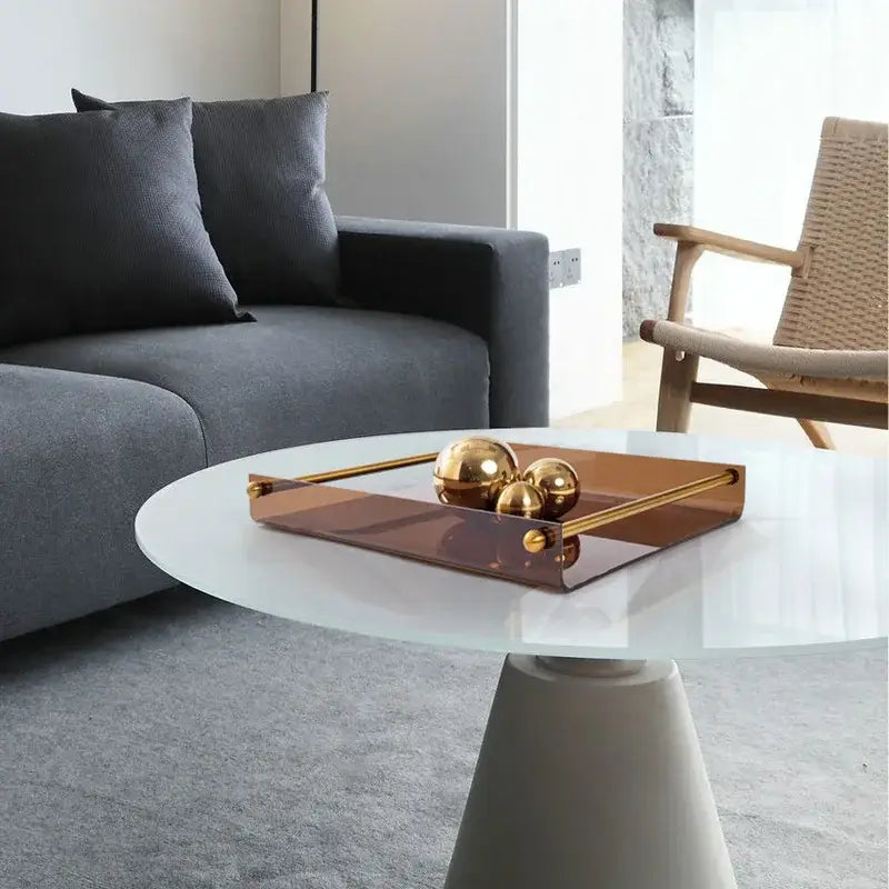 A modern amber acrylic fruit plate tray with polished gold-tone brass handles holds three reflective golden spheres