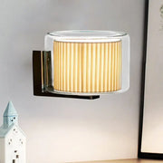 Modern wall lamp with pleated amber fabric shade, clear glass casing, and sleek black metal bracket for bedroom lighting