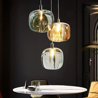 Three modern decorbites crystal led pendant lights in amber, green, and clear glass hang above a marble table