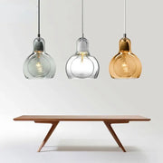 Three modern amber and gray glass pendant lights with bulbous shades hang above a minimalist wooden dining table