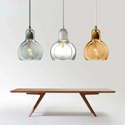 Three modern amber and gray glass pendant lights with bulbous shades hang above a minimalist wooden dining table