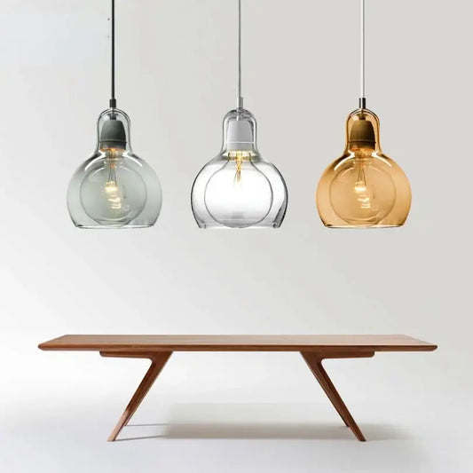 Three modern amber and gray glass pendant lights with bulbous shades hang above a minimalist wooden dining table