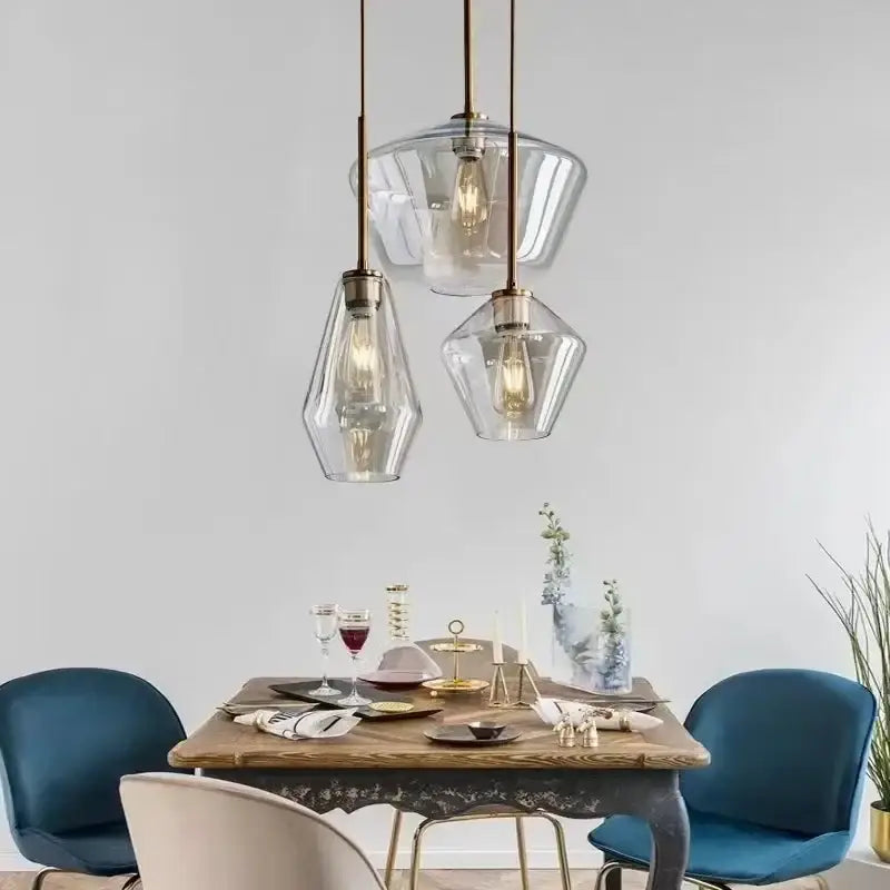 Three modern amber glass pendant lights with brass accents hang above a dining table in a living room chandelier design