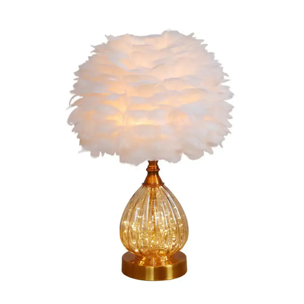 A warm-glowing decorbites modern amber glass droplet night light with a white feathered shade and textured base