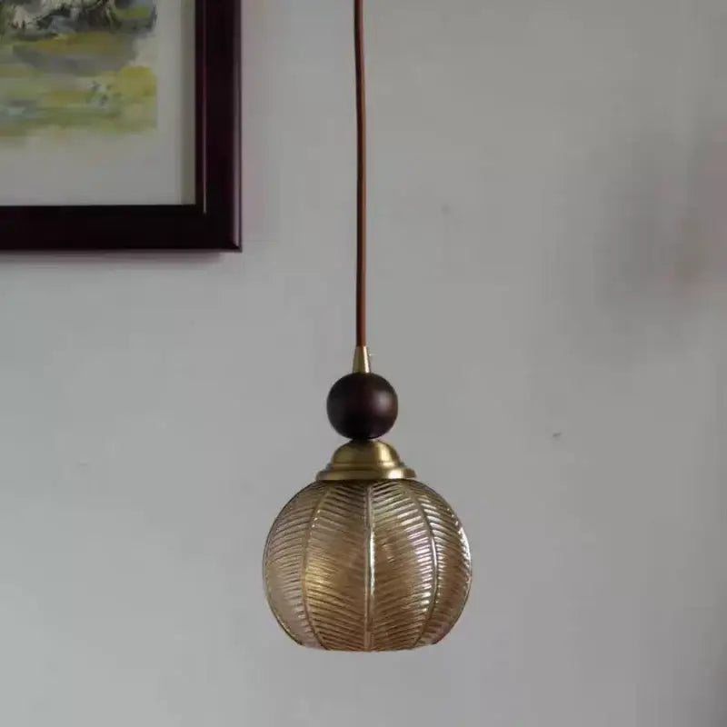 Modern amber glass led pendant light featuring a brass fixture with textured ribbed globe and dark wooden accent