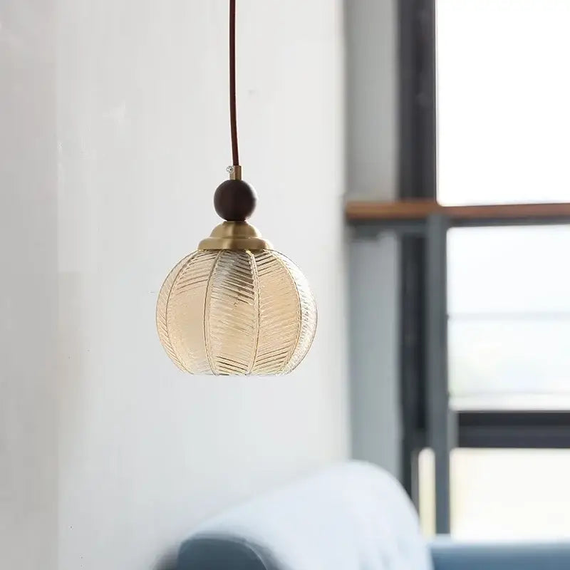 A modern amber glass led pendant light with brass fixture and dark wooden bead accent for dining room use