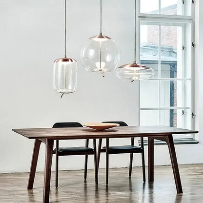 Three modern pendant lights with clear brokis knot glass globes and copper tops hang above a wooden dining table