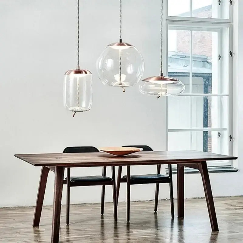 Three modern pendant lights with clear brokis knot glass globes and copper tops hang above a wooden dining table