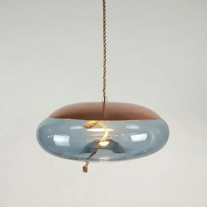A modern pendant light with translucent blue brokis knot glass and copper top suspended by a twisted gold cord for decorbites