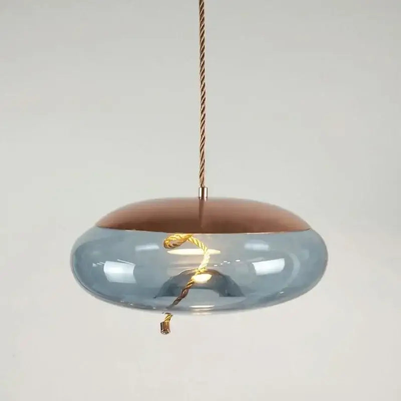 A modern pendant light with translucent blue brokis knot glass and copper top suspended by a twisted gold cord for decorbites