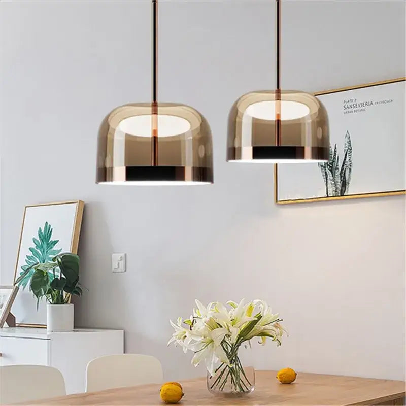 Two modern pendant lights with amber glass shades and copper finish metal frames for dining room use