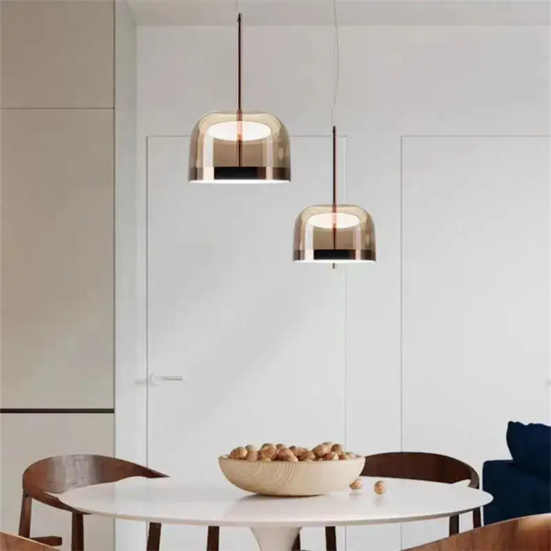 Two modern amber glass pendant lights with copper finish hang above a white dining table in a dining room setting