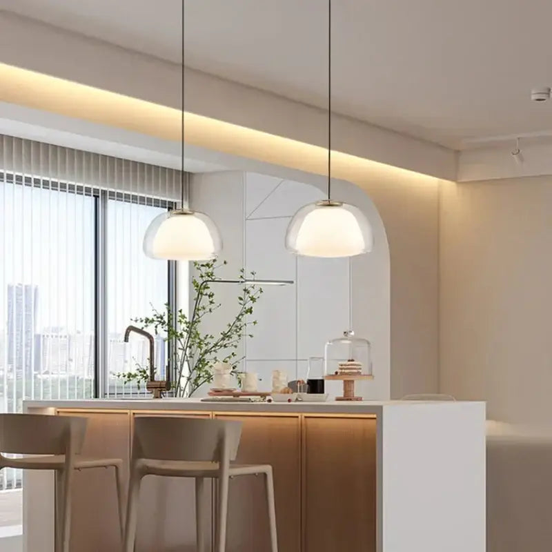 Two modern amber and gray glass pendant lights with frosted shades hang above a kitchen island with thin black cords