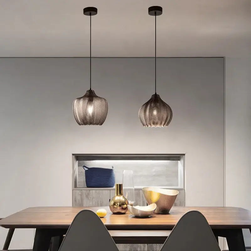 Two sleek dark-toned amber gray glass pendant lights with woven mesh shades hang above a wooden dining table decorbites amber gray