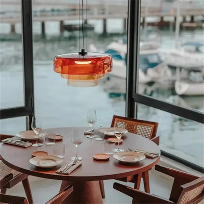 A modern amber layered glass pendant light with translucent shades hangs above a wooden dining table decorbites levels colorful