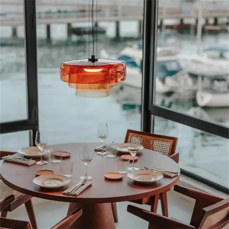 A modern amber layered glass pendant light with translucent shades hangs above a wooden dining table decorbites levels colorful