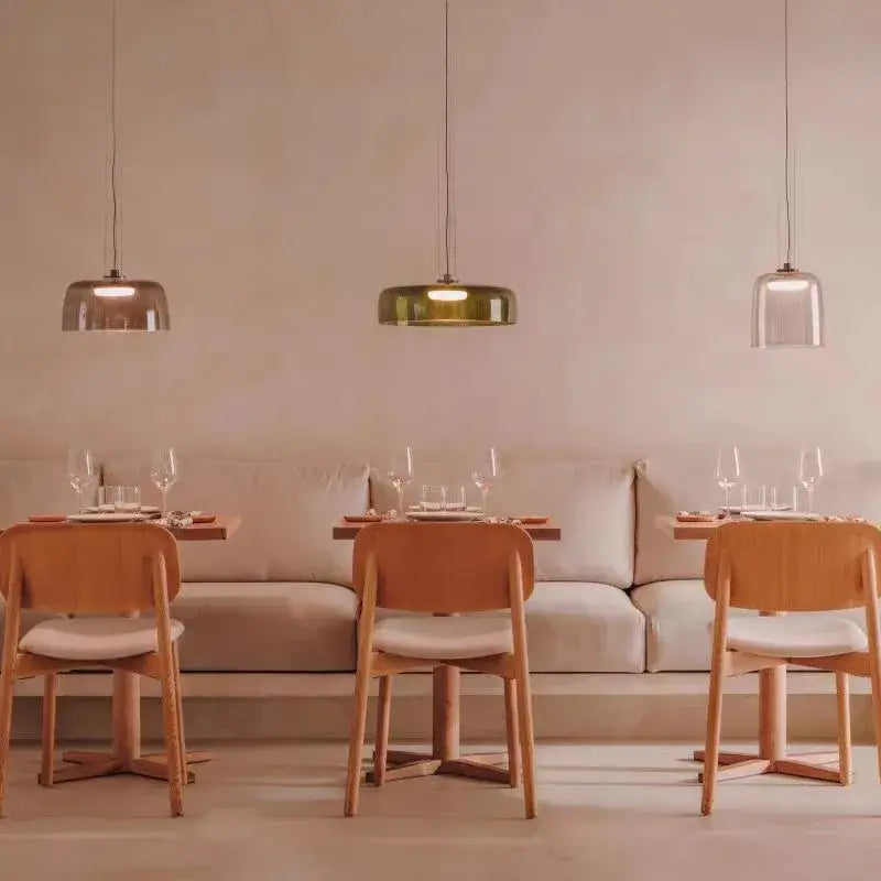 Three modern amber layered glass pendant lights with metallic shades hang above a minimalist dining area decorbites levels colorful glass