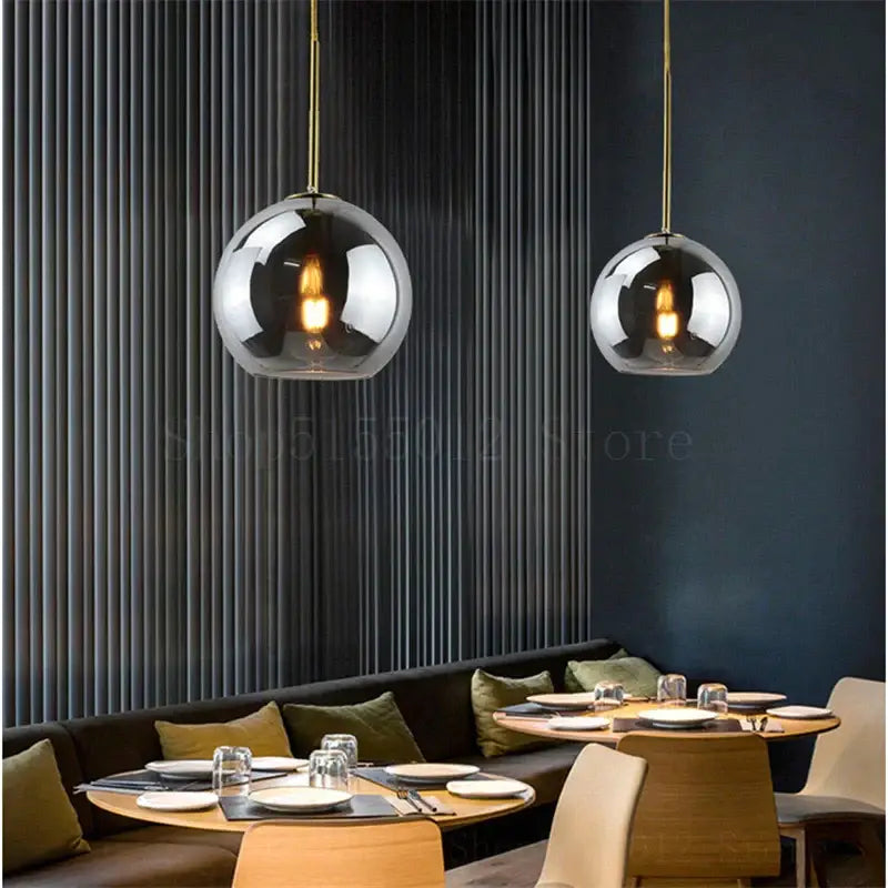 Two amber smoked gray and clear glass ball led pendant lights with brass chains hang above a dining table decorbites glass ball