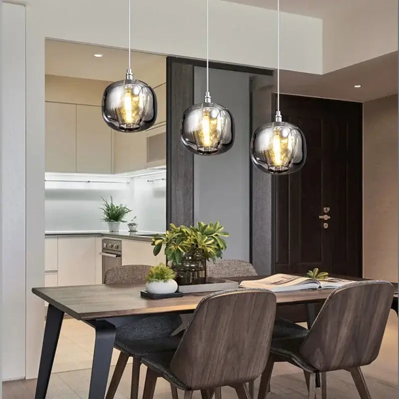 Modern amber and smoky grey crystal staircase chandelier features three spherical glass pendant lights with metallic sheen above dining table