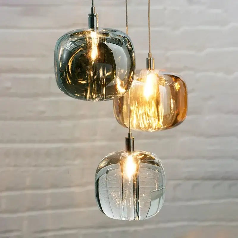 Three modern amber and smoky grey crystal staircase chandelier pendant lights with textured glass hang against a white brick wall