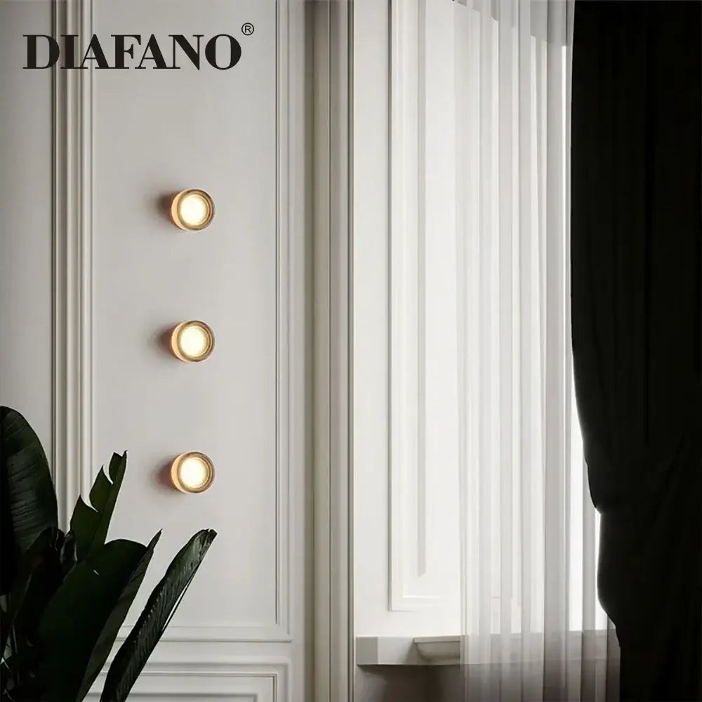 Three circular gold-toned modern amber and white glass sconce led wall lamps for elegant living room lighting
