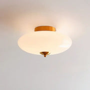 A sleek modern bauhaus cream white ceiling lamp with brass finish and cream white glass shade for bedroom lighting