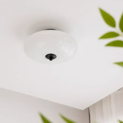 A sleek bauhaus cream white glass ceiling lamp with white frosted glass and black central fixture for bedroom use