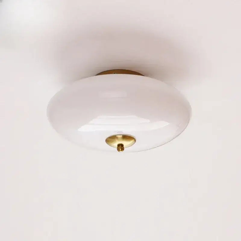 A modern bauhaus cream white glass ceiling lamp with sleek opaline glass and brass-finished base for bedroom use