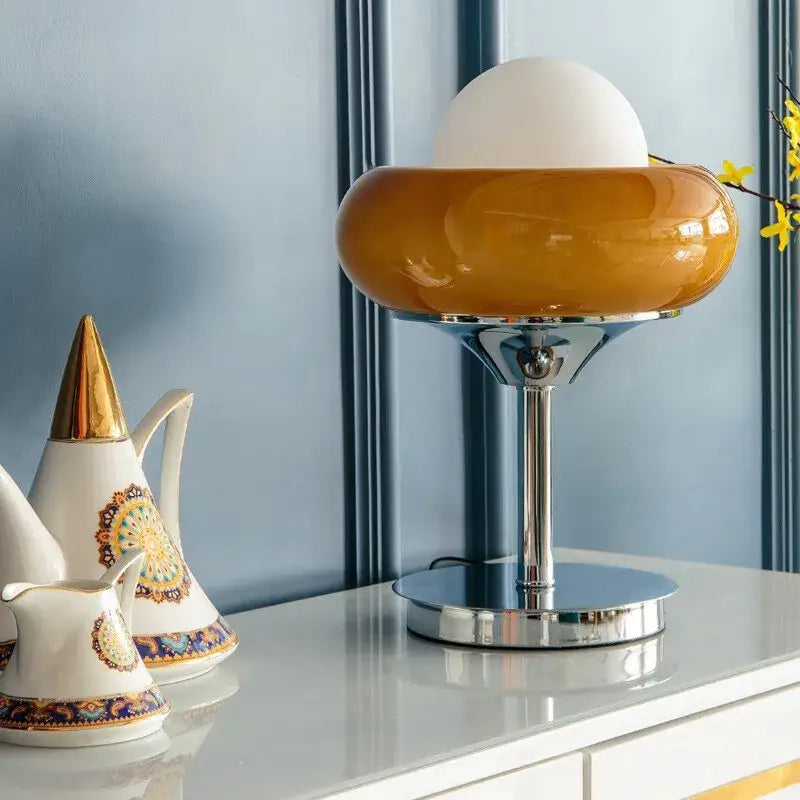 A sleek guzzini modern bauhaus table lamp with glossy amber glass base and white spherical shade on chrome stem