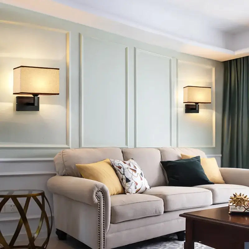 Beige upholstered sofa with rolled arms and nailhead trim displayed alongside decorbites hotel fabric wall lamp