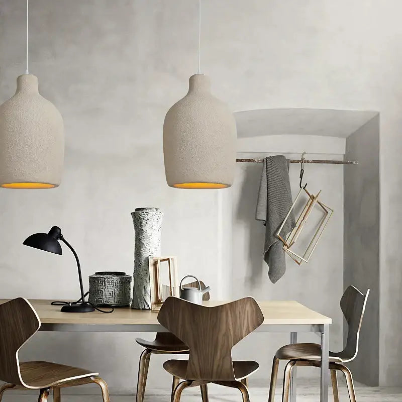 Two beige textured decorbites cement led chandelier pendant lights with warm yellow interiors hang above a dining table