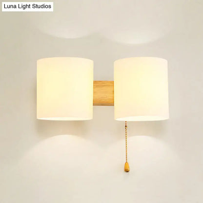 Minimalist modern beige fabric and wood wall light bedroom sconce with two shades and brass pull chain on wood bar