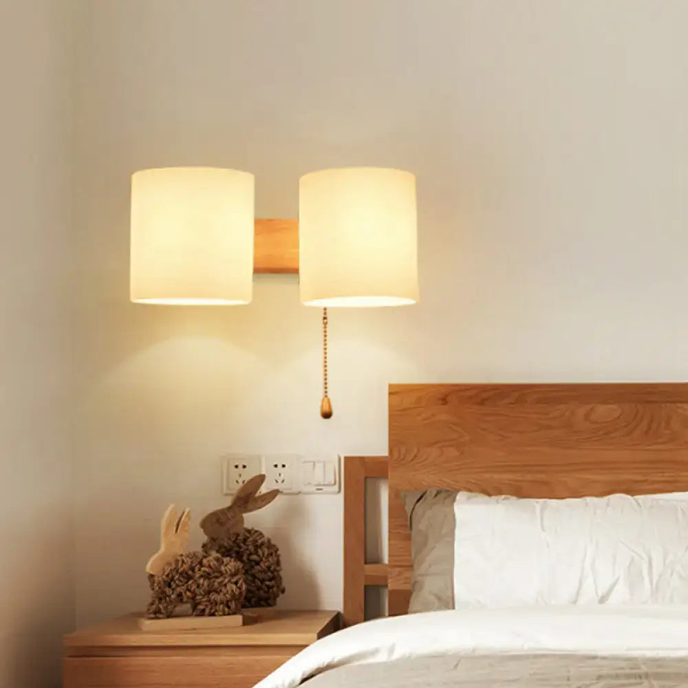 Modern beige fabric and wood wall light bedroom sconce with warm-toned cylindrical lampshade and pull chain switch