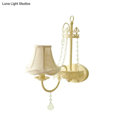 Cream-colored wrought iron modern beige ornate crystal wall sconce with floral cutouts and fabric shade 15 inch fixture